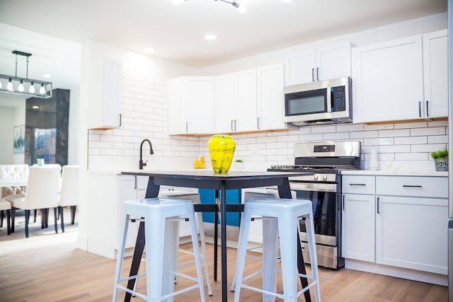 118 W 118th St, Chicago, IL 60628 - kitchen with appliances with stainless steel finishes, backsplash, white cabinets, light countertops, and light wood-style floors