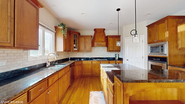 kitchen with stainless steel appliances, a sink, premium range hood, and brown cabinetry
