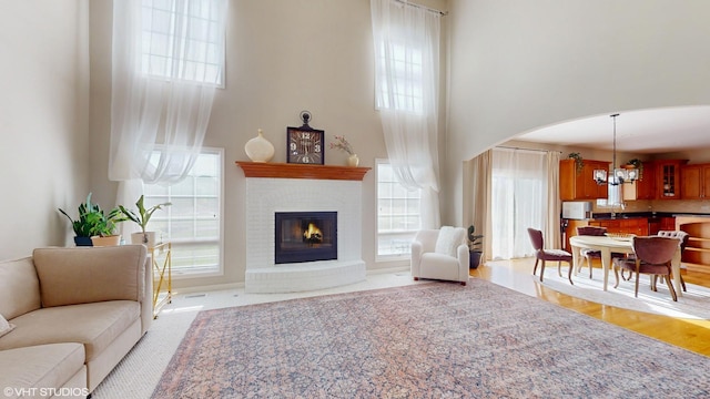 living room featuring a towering ceiling, arched walkways, a chandelier, and a fireplace