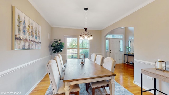 dining area with a chandelier, light wood-style flooring, arched walkways, and ornamental molding