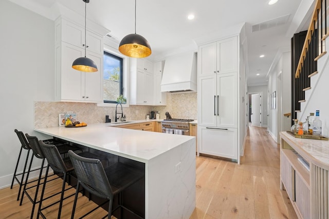 kitchen with custom exhaust hood, a peninsula, a kitchen bar, light wood-type flooring, and recessed lighting