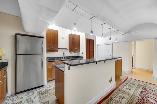 kitchen with freestanding refrigerator, a sink, a center island, brown cabinetry, and vaulted ceiling