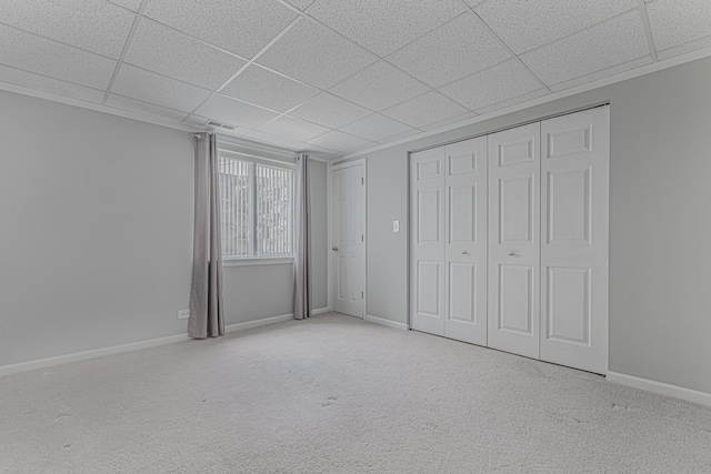 unfurnished bedroom featuring a paneled ceiling, carpet, baseboards, and a closet