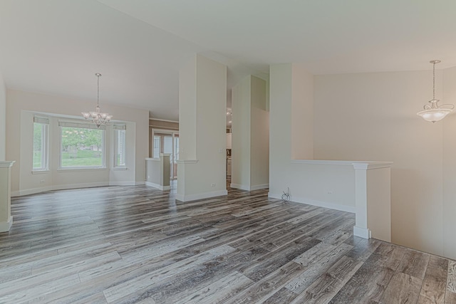 spare room featuring wood finished floors, a chandelier, baseboards, and lofted ceiling