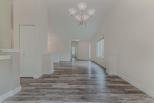 unfurnished dining area with high vaulted ceiling, a chandelier, wood finished floors, and baseboards