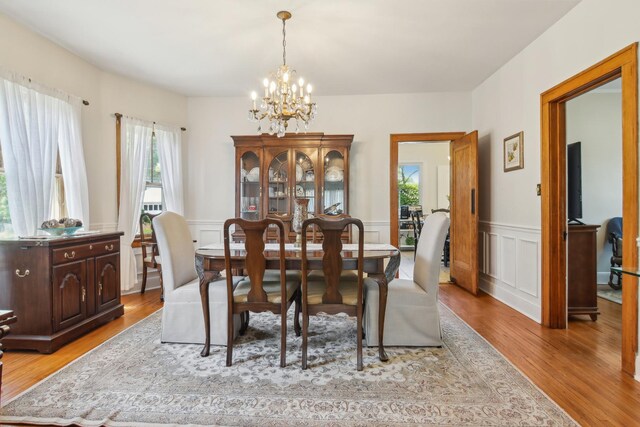 dining space featuring a chandelier, plenty of natural light, light wood-style flooring, a wainscoted wall, and a decorative wall