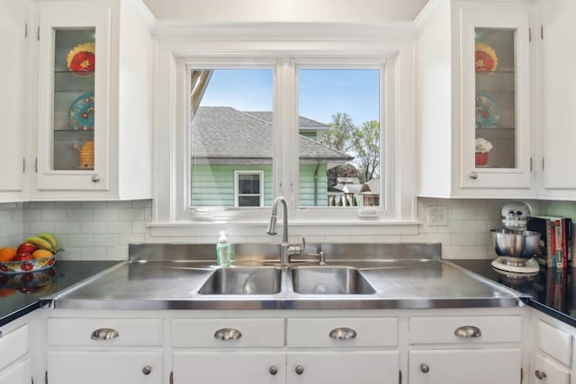 kitchen with stainless steel countertops, white cabinets, a sink, and crown molding