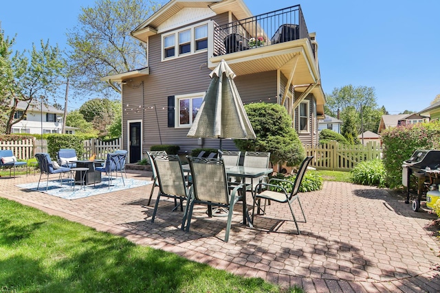 rear view of house featuring a balcony, fence, a patio area, and outdoor dining space