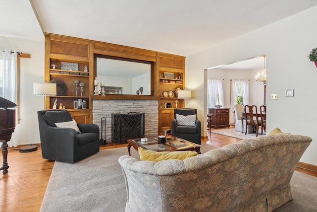 living room with light wood-style floors, a chandelier, and a stone fireplace