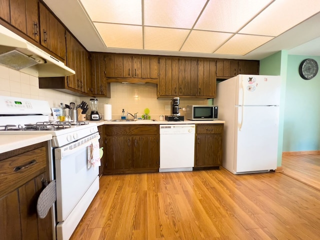 kitchen with white appliances, under cabinet range hood, a sink, light countertops, and backsplash