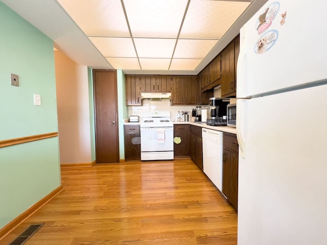kitchen with white appliances, under cabinet range hood, light countertops, a paneled ceiling, and light wood-type flooring