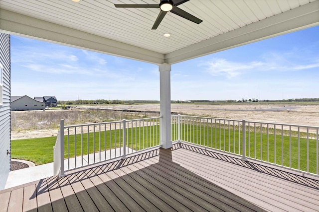 wooden terrace featuring ceiling fan, a lawn, and a view of countryside