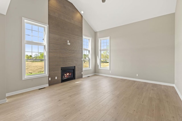 unfurnished living room with high vaulted ceiling, baseboards, light wood-style floors, and a fireplace