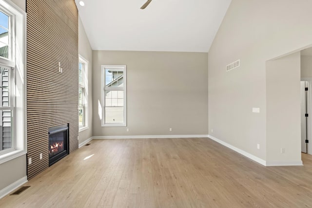 unfurnished living room with light wood finished floors, baseboards, a tile fireplace, and high vaulted ceiling
