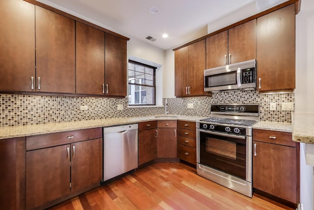 kitchen featuring stainless steel appliances, light wood-style flooring, a sink, light stone counters, and decorative backsplash