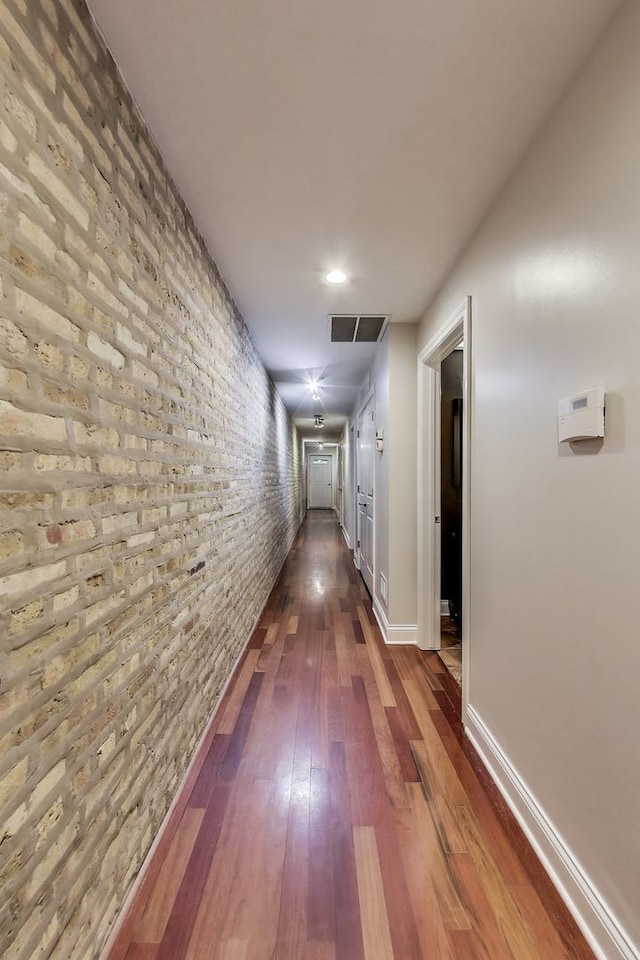 hall with dark wood-type flooring, brick wall, and baseboards