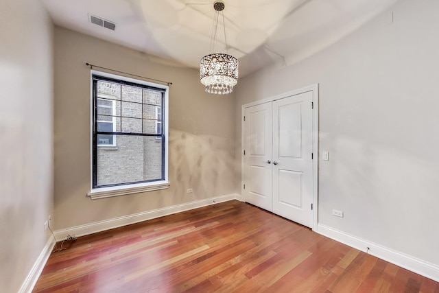 spare room featuring a chandelier, wood finished floors, and baseboards
