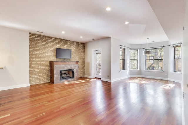 unfurnished living room with a brick fireplace, light wood finished floors, brick wall, baseboards, and recessed lighting