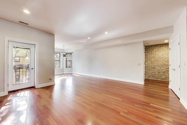 unfurnished living room featuring light wood finished floors, baseboards, brick wall, and recessed lighting