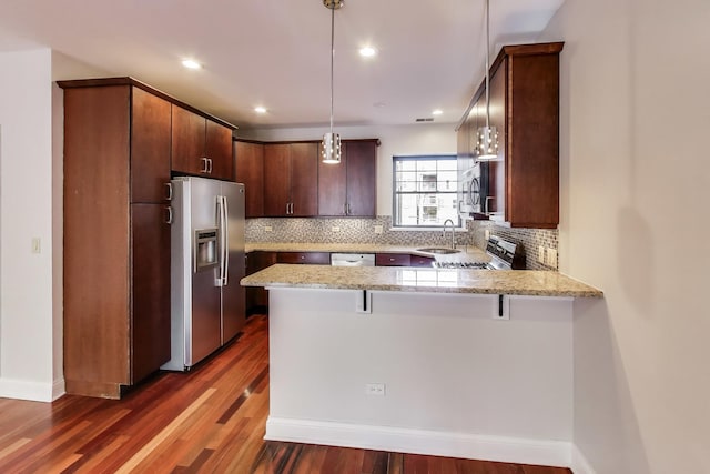 kitchen with appliances with stainless steel finishes, a peninsula, a sink, backsplash, and recessed lighting