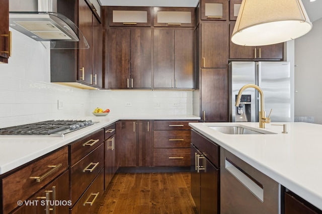 kitchen featuring wall chimney exhaust hood, appliances with stainless steel finishes, light countertops, dark wood finished floors, and a sink