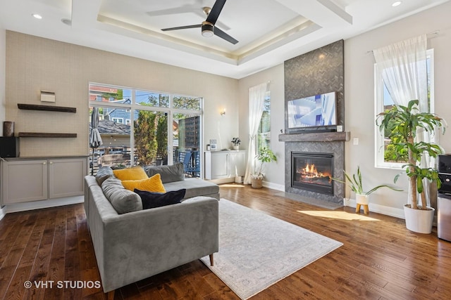 living room with a fireplace, ceiling fan, a tray ceiling, dark wood finished floors, and recessed lighting