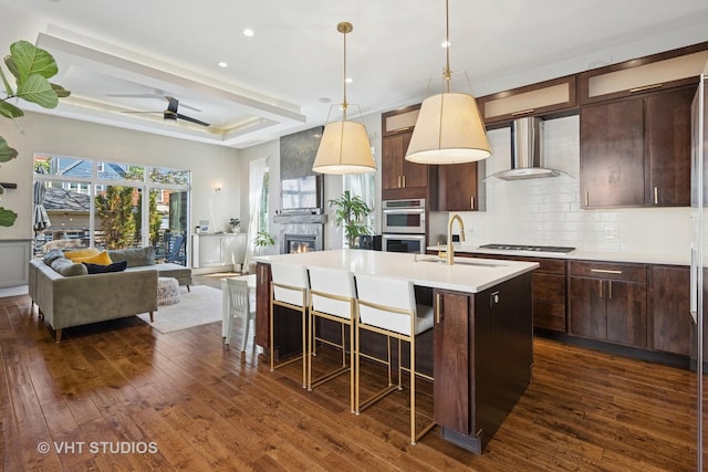 kitchen with a sink, wall chimney exhaust hood, dark wood-type flooring, decorative backsplash, and recessed lighting