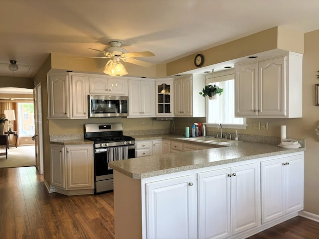 kitchen featuring stainless steel appliances, a sink, a peninsula, a ceiling fan, and dark wood finished floors