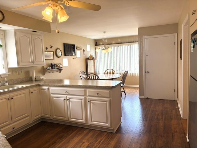 kitchen featuring a peninsula, a sink, ceiling fan, dark wood-style floors, and white cabinetry