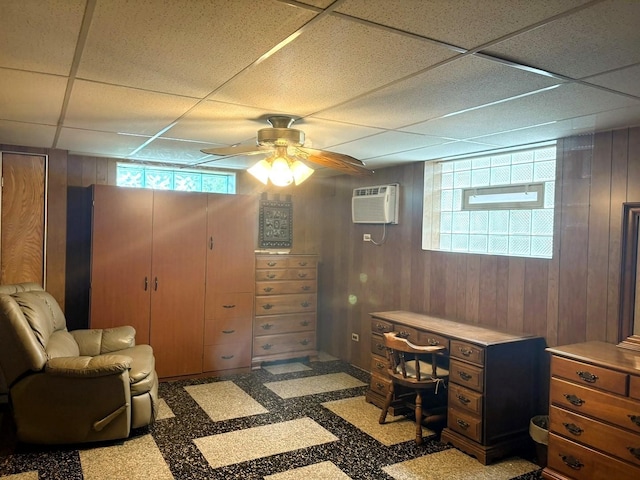 office area with a drop ceiling, an AC wall unit, ceiling fan, and wood walls