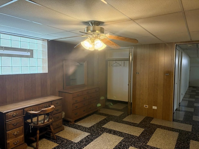 office area featuring wood walls, ceiling fan, and a paneled ceiling