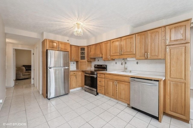 kitchen with appliances with stainless steel finishes, a sink, light countertops, premium range hood, and glass insert cabinets
