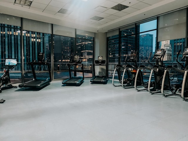 gym with a paneled ceiling, floor to ceiling windows, and a city view