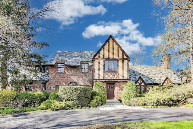 tudor-style house with brick siding, a chimney, and a high end roof