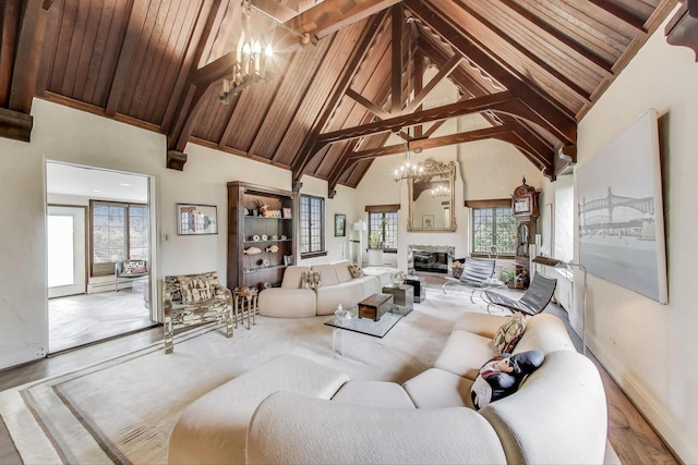 living area featuring a chandelier, high vaulted ceiling, baseboards, beam ceiling, and a glass covered fireplace