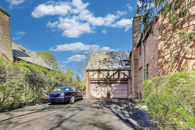 view of side of home featuring brick siding, driveway, a high end roof, a chimney, and a garage