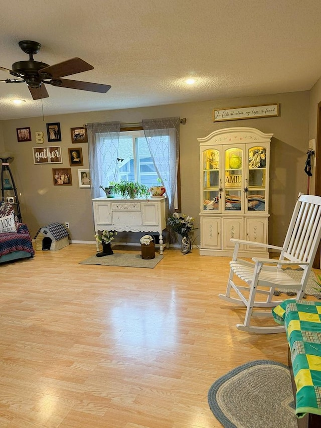 sitting room featuring ceiling fan, light wood-type flooring, a textured ceiling, and baseboards