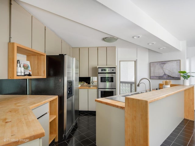 kitchen featuring wood counters, stainless steel appliances, dark tile patterned flooring, a sink, and cream cabinets