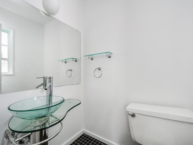 half bathroom featuring a sink, baseboards, toilet, and tile patterned floors