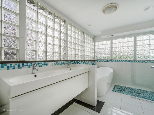bathroom with tile walls, tile patterned flooring, a freestanding bath, and double vanity