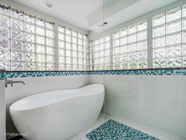 full bath with tile walls, tile patterned flooring, a soaking tub, and a walk in shower