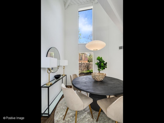 dining room with plenty of natural light, wood finished floors, baseboard heating, a high ceiling, and beam ceiling