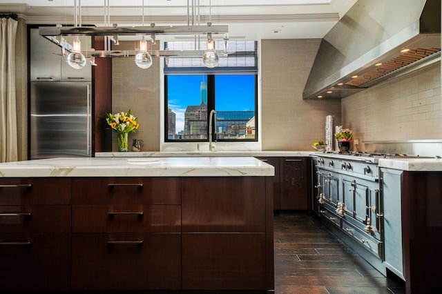 kitchen featuring wall chimney range hood, a sink, dark wood-style floors, dark brown cabinetry, and light stone countertops