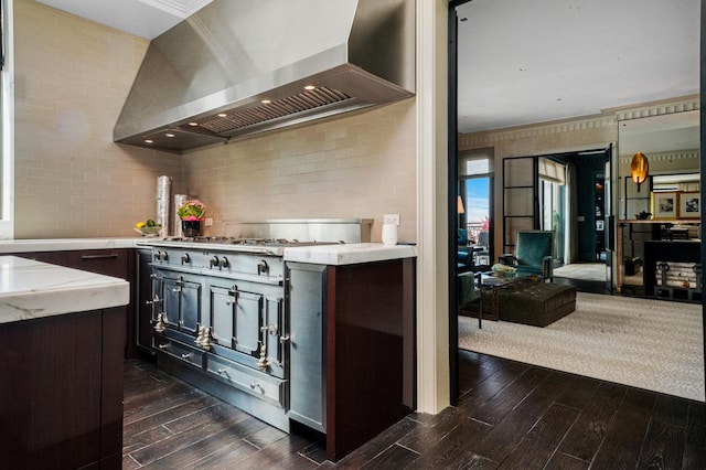 kitchen featuring wall chimney range hood, dark wood-style floors, backsplash, dark brown cabinetry, and ornamental molding