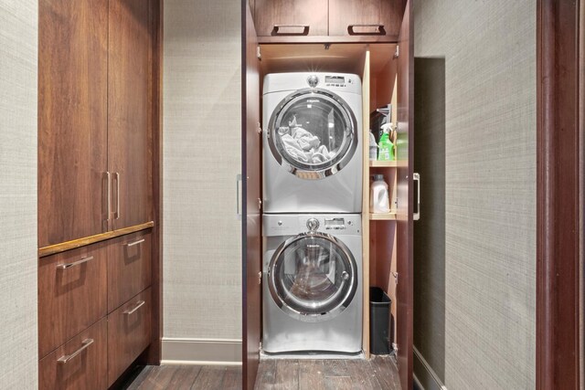 laundry area with stacked washer / drying machine, wood finished floors, and baseboards