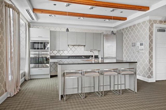 kitchen featuring appliances with stainless steel finishes, gray cabinetry, dark countertops, carpet flooring, and beam ceiling
