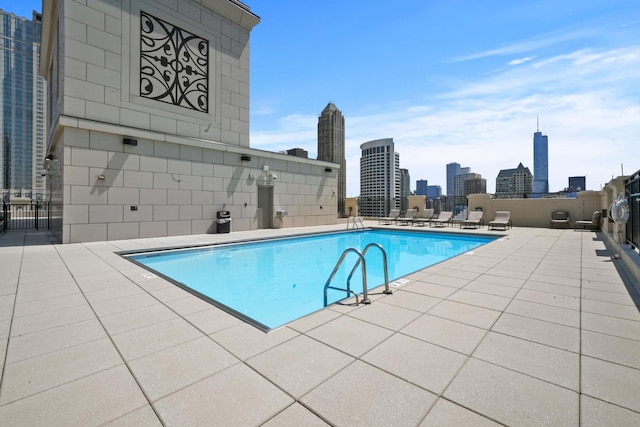 community pool with a patio, a view of skyline, and fence