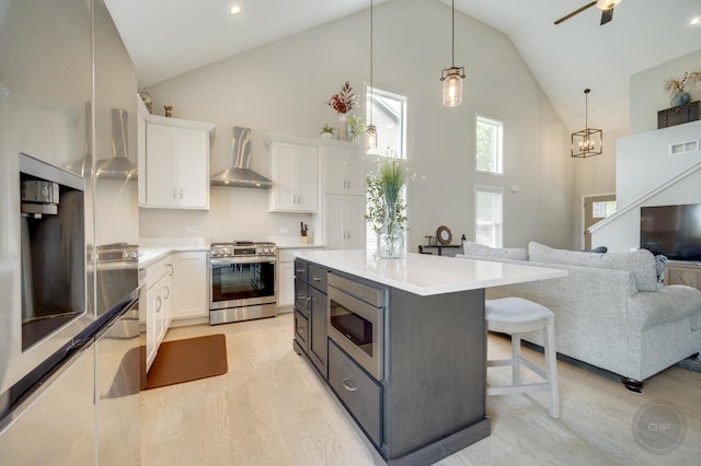 570 Sudbury Cir, Oswego, IL 60543 - kitchen with appliances with stainless steel finishes, wall chimney exhaust hood, high vaulted ceiling, white cabinets, and a kitchen bar
