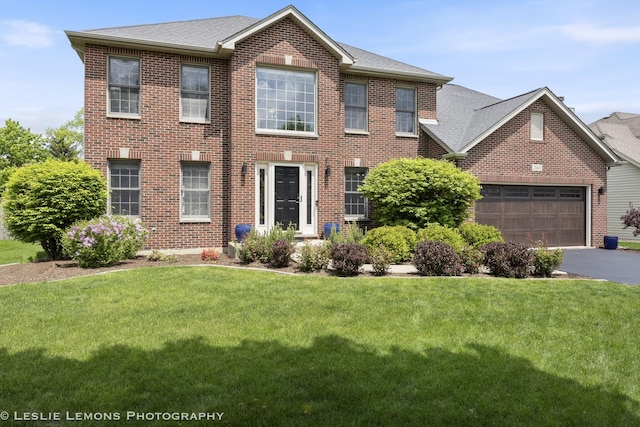 view of front of home with brick siding, a front yard, a garage, driveway, and roof with shingles
