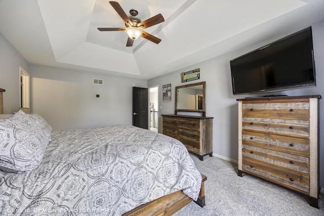 bedroom with a raised ceiling, light colored carpet, and a ceiling fan